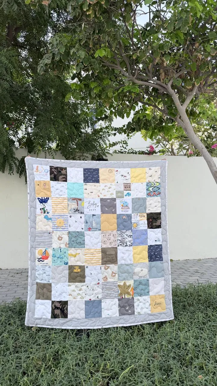 Memory quilt made from baby clothes, held up outdoors under a tree